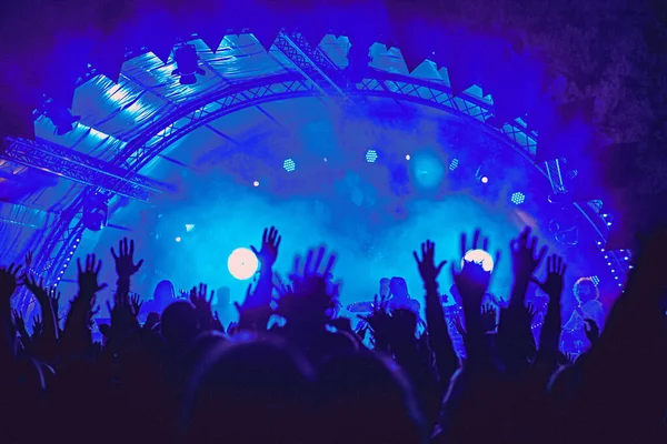 要旨ぼやけた雰囲気 野外音楽祭コンサートを楽しむ幸せな人々 手を上げて喜びの拍手 活発なナイトライフの概念 巨大なステージでの光と影の遊び — ストック写真