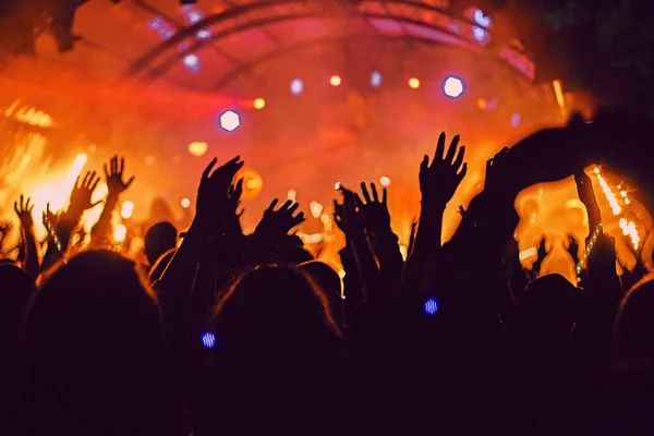 Abstract blur atmosphere: happy people enjoying outdoor music festival concert, raised up hands and clapping of pleasure, active night life concept, play of light and shadow on the huge stage