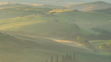 Tuscany, İtalya - 10 Haziran 2018: Puslu tepelik Tuscan alanında bir çiftlik ve selvi ile Valdocia, Orta Italya'nin akşam altın saatte görünümünü