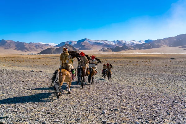 Mongolian Eagle Hunter in tradition clothes on horseback riding to The Golden Eagle Festival Competition Site at Ulgii in Mongolia