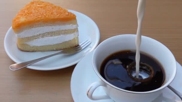 用一块蛋糕在白色盘子里 慢慢地把新鲜的牛奶倒进一杯咖啡里 — 图库视频影像