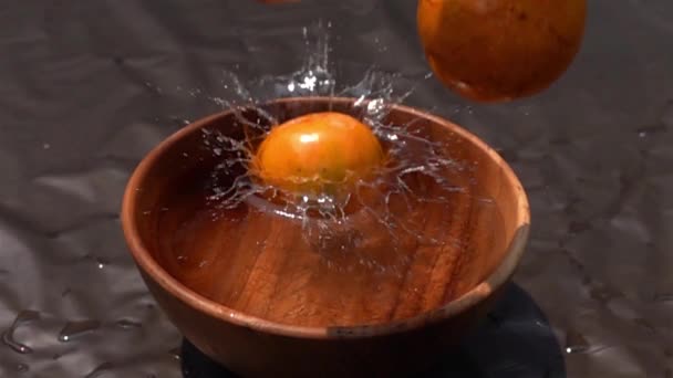 スローモーションで暗い背景に木製のボウルに水に落ちるオレンジ — ストック動画