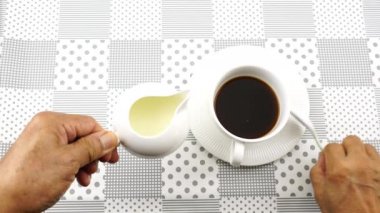 Adam sütsüz kahve bardağına taze süt döker ve masa örtüsünde karıştırır..