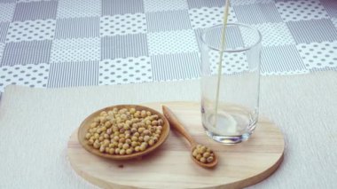 Tahta bir tahta tabakta soya fasulyesi yığını ve tahta bir kaşıkla birlikte tahtadan bir tahtanın üzerine ev yapımı soya sütü veya soya fasulyesi sütü dökün. Soya fasulyesi insanlar için çok önemli bir bitki proteinidir..