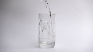 Yavaş çekimde beyaz arka planda içme bardağına su dökün.