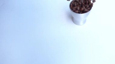 Kahve çekirdekleri ile dolu alüminyum bardak beyaz zemine yavaşça düşer..