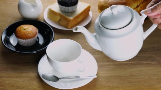 木製のトレイにパンのローフと白いセラミックカップに黒コーヒーを注ぎ 白いプレートにパンのスライス 木製のテーブルの上に黒いプレートにマフィン — ストック動画