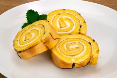 Tahta bir masada beyaz seramik tabakta dilimlenmiş kek rulosu yığını..