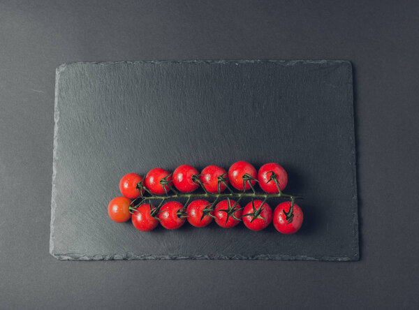 branch of fresh tomatoes cherry on a stone black background 