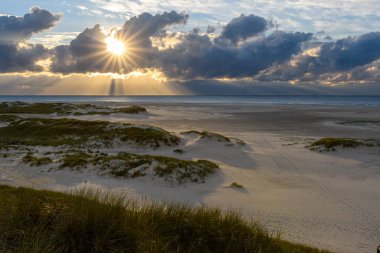 Amrum Adası, Almanya: güneş ışınları Amrum sahilindeki kara fırtına bulutlarından doğuyor. Gün batımı yoğun bir bulut yüzünden bulanıklaşır ve hava kötüleşir.