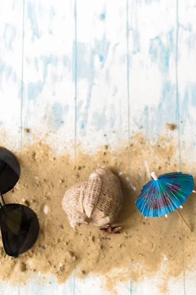 海滩静物。黑色眼镜与鸡尾酒伞, 贝壳在沙子上的木质背景 — 图库照片