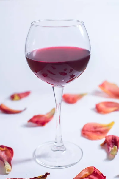 Красное вино на белом фоне с лепестками роз — стоковое фото