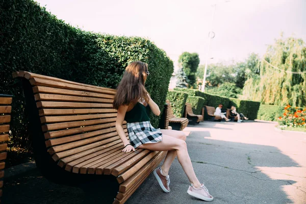 Uma menina em uma camisa preta e shorts em um parque em um banco — Fotografia de Stock