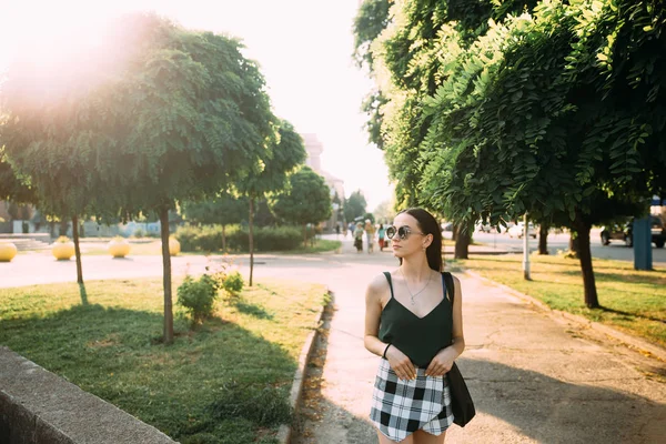 Barna lány, egy nyári nap a városban, kerek napszemüveget visel — Stock Fotó