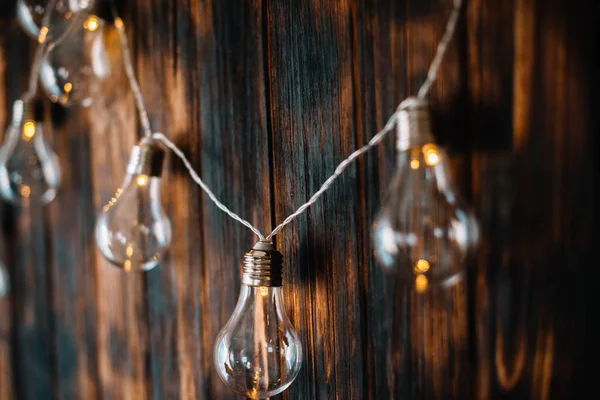 Light bulbs hang on dark wooden wall — Stock Photo, Image