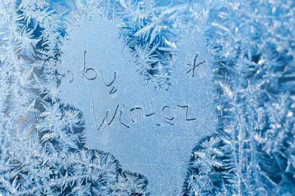 A inscrição: adeus, inverno. Em uma janela de inverno congelada em padrões gelados — Fotografia de Stock