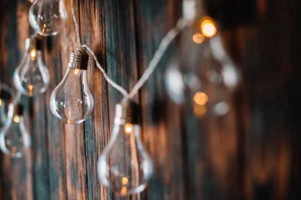Light bulbs hang on dark wooden wall — Stock Photo, Image