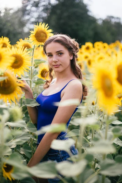 Vacker flicka på fältet med solrosor i korta shorts och en väst — Stockfoto