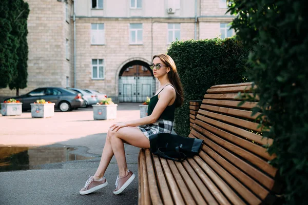 Uma menina em uma camisa preta e shorts em um parque em um banco — Fotografia de Stock