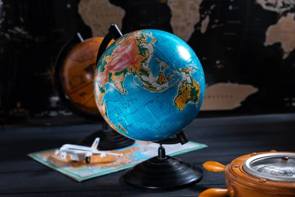 Globo con un barómetro y un pequeño avión en el fondo de un mapa del mundo negro — Foto de Stock