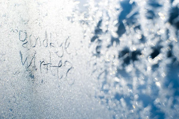 A inscrição: adeus, inverno. Em uma janela de inverno congelada em padrões gelados — Fotografia de Stock