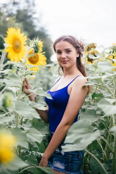 Vacker flicka på fältet med solrosor i korta shorts och en väst — Stockfoto