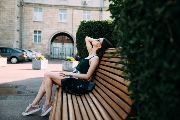 Uma menina em uma camisa preta e shorts em um parque em um banco — Fotografia de Stock