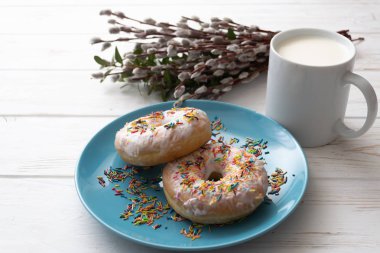 Bir fincan süt beyaz ahşap zemin üzerinde mavi bir tabakta donut