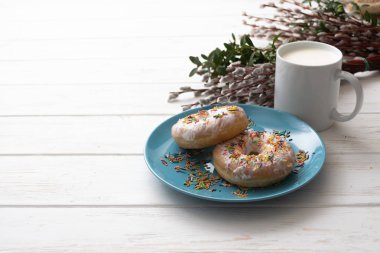 Bir fincan süt beyaz ahşap zemin üzerinde mavi bir tabakta donut