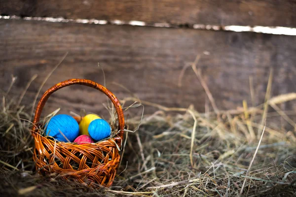 Uova di Pasqua in un cesto su un fieno con uno sfondo sfocato — Foto Stock