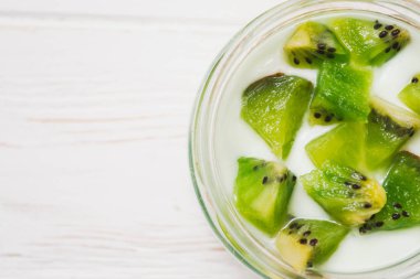 Kivi dilimleri ahşap beyaz zemin üzerine yoğurtlu.