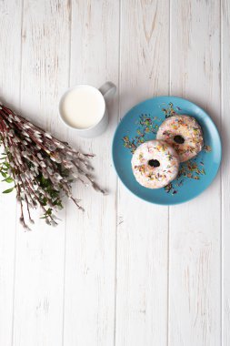 Donuts bir fincan süt ve willow dallar ile beyaz ahşap zemin üzerinde