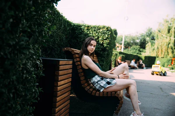 年轻女孩摆姿势在绿色公园现场坐在长凳上 — 图库照片