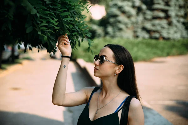 Barna lány, egy nyári nap a városban, kerek napszemüveget visel — Stock Fotó