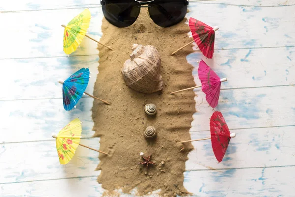 海滩静物。黑色眼镜与鸡尾酒伞, 贝壳在沙子上的木质背景 — 图库照片