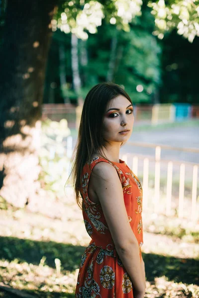 Beautiful young girl in a summer red dress in a park — Stock Photo, Image