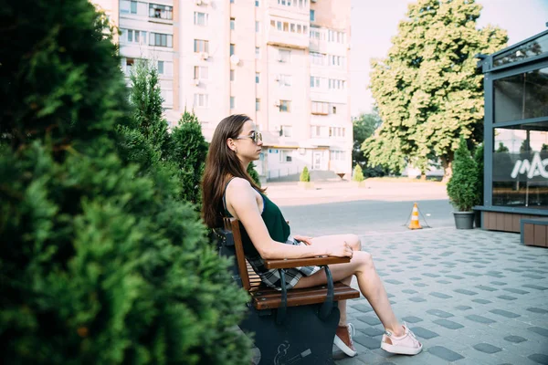 Uma menina em uma camisa preta e shorts em um parque em um banco — Fotografia de Stock