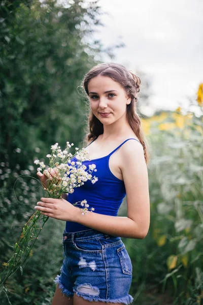 En flicka i korta shorts och en blå T-shirt med en bukett av vilda blommor — Stockfoto