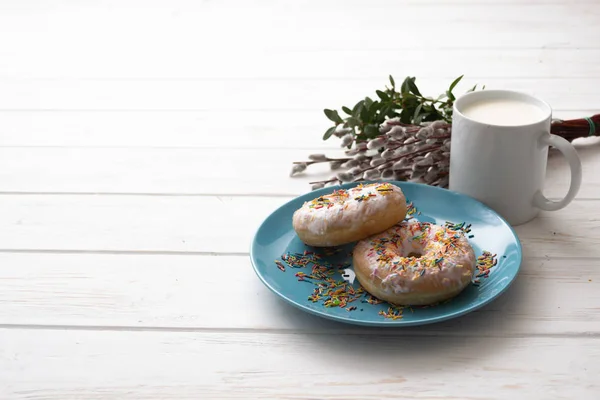 Ciambelle su un piatto blu con una tazza di latte su uno sfondo di legno bianco — Foto Stock