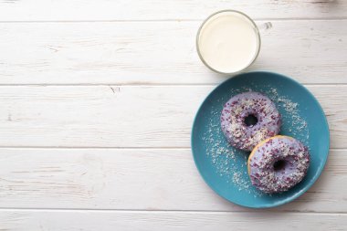 Bir fincan süt beyaz ahşap zemin üzerinde mavi bir tabakta donut