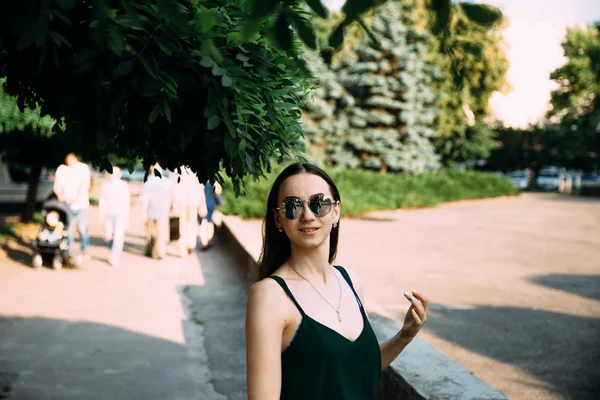 Chica morena en un día de verano en la ciudad con gafas de sol redondas —  Fotos de Stock