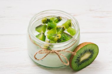 Kivi dilimleri ahşap beyaz zemin üzerine yoğurtlu.