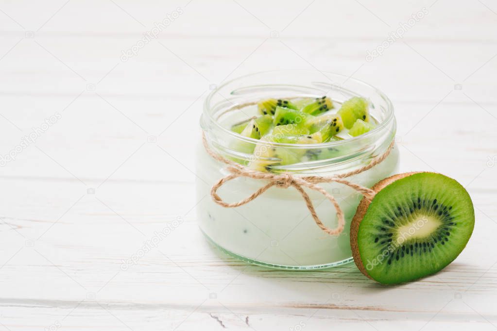 Yogurt with kiwi slices on a wooden white background.