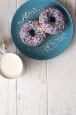 Bir fincan süt beyaz ahşap zemin üzerinde mavi bir tabakta donut