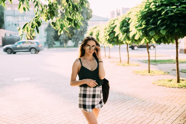 Chica morena en un día de verano en la ciudad con gafas de sol redondas —  Fotos de Stock