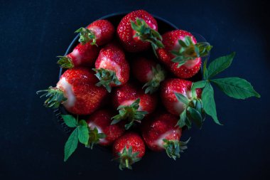 Siyah bir arka planda siyah bir tabakta taze sulu çilekler.