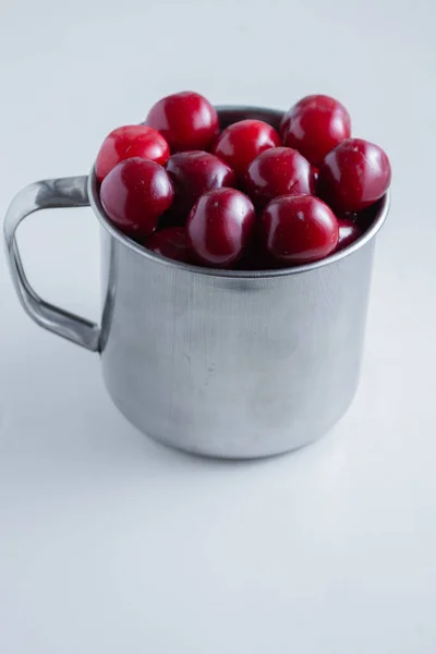 Cerejas doces em uma caneca de aço em um fundo de papel branco — Fotografia de Stock