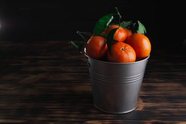 Tahta bir arka planda kovada yaprakları olan taze mandalinalar.