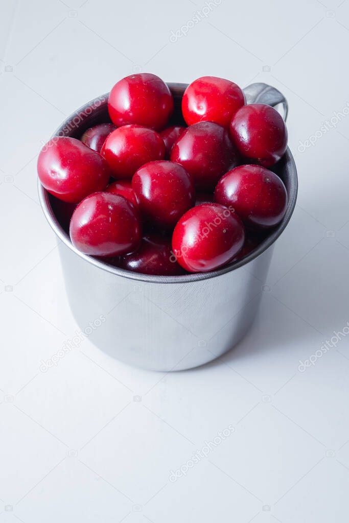 Sweet cherries in a steel mug on a white paper background