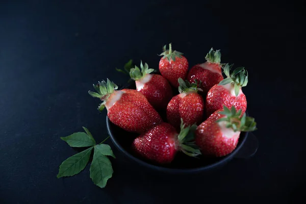 Fresh juicy strawberries in a black plate on a black matte background
